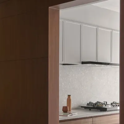 A glimpse into the kitchen, framed by a terracotta lime-washed wall. The design features light grey cabinets and a terrazzo backsplash, blending earthy charm with modern functionality.