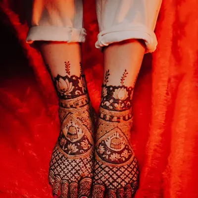 An artistic shot of the bride's feet, adorned with stunningly detailed mehndi designs against a vibrant red background.