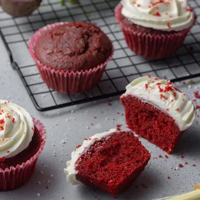 Red velvet cupcakes with cream cheese frosting. The composition includes a cut-open cupcake to show the moist, vibrant crumb, a key detail for bakery photography.
