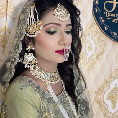 An elegant Muslim bridal look in a light green outfit. The makeup features a soft green smokey eye and a bold red lip, paired with a classic side-swept hairstyle and traditional jewellery.