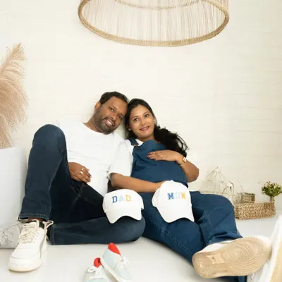 A relaxed, casual portrait of a couple in coordinating denim and white. Props like baby shoes and 'Mom' and 'Dad' caps make the shoot personal and fun.