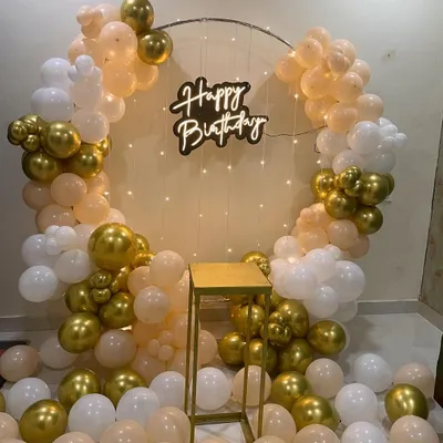 This chic birthday backdrop features a circular frame with a delicate arch of peach, white, and gold balloons. The "Happy Birthday" neon sign and scattered floor balloons complete this perfect photo corner for any birthday party.