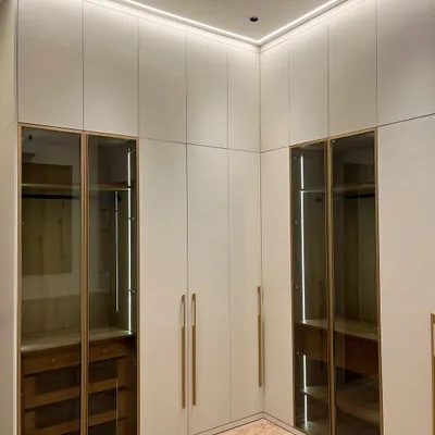 A custom L-shaped wardrobe designed for a master bedroom in Ambala. The combination of closed cabinets and tinted glass doors with internal lighting offers both hidden storage and a beautiful display.