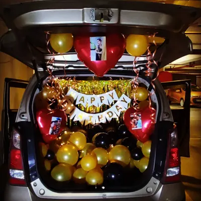 A personalized car trunk birthday surprise. This setup includes black and gold balloons, a 'Happy Birthday' banner, and custom heart-shaped balloons featuring photos of the birthday person.