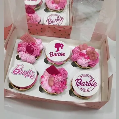 A box of custom Barbie-themed cupcakes, perfect for a birthday girl. Each cupcake is 100% eggless, with some featuring detailed edible prints and others topped with pink frosting, sprinkles, and chocolate pieces for a truly magical look.