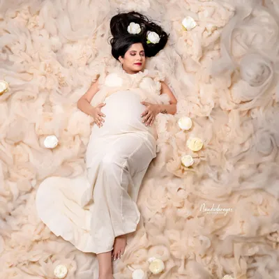 A dreamy and artistic top-down shot, with the mother-to-be lying in a bed of soft, cloud-like fabric and white roses. This is a truly unique and ethereal maternity portrait.