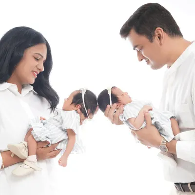 A beautiful, symmetrical portrait of parents holding their newborn twin girls. This pose highlights the joy and wonder of having two new babies to love.