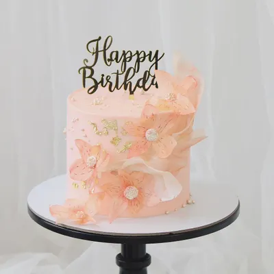 An ethereal and delicate birthday cake. This soft pink cake is adorned with translucent, handcrafted rice paper flowers and touches of gold leaf, creating a light and airy design.