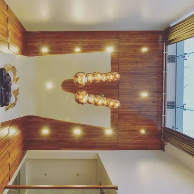 The ceiling of a double-height living room in a high-end villa in Bengaluru. The design features warm wood paneling and a dramatic chandelier, illustrating our belief that "God is in the details."