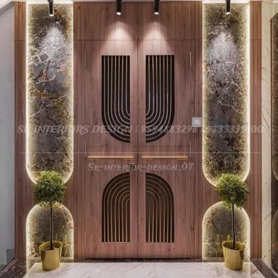 A grand entrance featuring a double door with modern semi-circular grooves. The doors are flanked by marble panels and illuminated niches with planters, creating a luxurious first impression.
