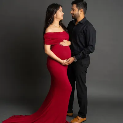 A classic studio portrait for you and your partner. The mom-to-be wears a striking red off-the-shoulder gown, creating a beautiful contrast with her partner's all-black attire as they share a loving gaze.