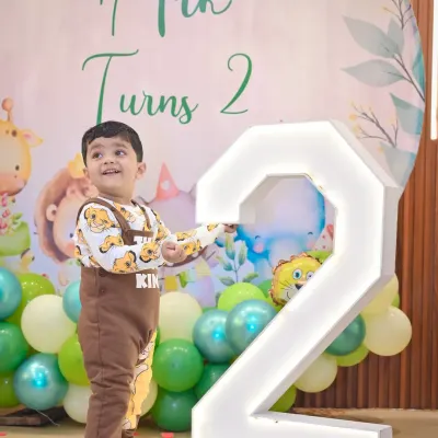 The birthday boy proudly stands next to a giant light-up number '2' at his jungle-themed party.