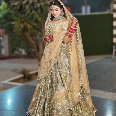 A full-length view of a magnificent golden sequin lehenga. The pearl-bordered dupatta and green-accented jewellery add a touch of classic elegance.