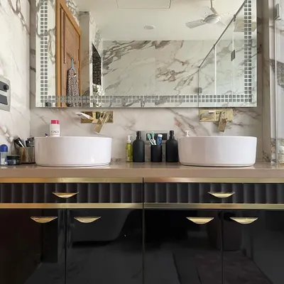 This bathroom features a stunning double vanity set against a wall of Calacatta marble. The glossy black drawers with gold hardware provide a bold contrast, creating a high-end, hotel-like feel.