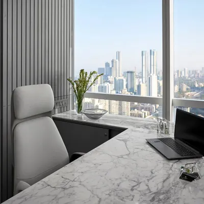 An office with a view. This executive cabin features a clean, white marble desk and a comfortable, ergonomic chair, all positioned to take full advantage of the panoramic city skyline. It’s a space designed for focus and inspiration.