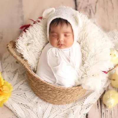 A vision in white. This classic newborn portrait features a baby sleeping peacefully in a basket, wearing an adorable bear bonnet and surrounded by soft, spring-like details.