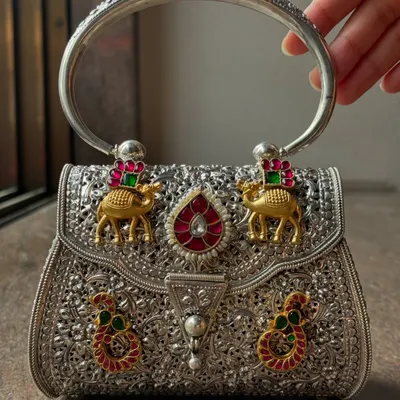 Our stunning fusion silver handbag, held to showcase its solid round handle and detailed craftsmanship. The bag features gold-plated camel motifs and colourful stone work, making it a true work of art.