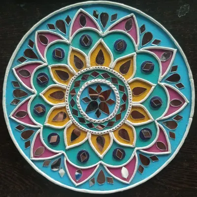 A close-up of a finished Lippan art piece with a floral mandala design. Notice how the combination of bright turquoise, yellow, and pink paint with carefully placed mirrors creates a vibrant, eye-catching effect.