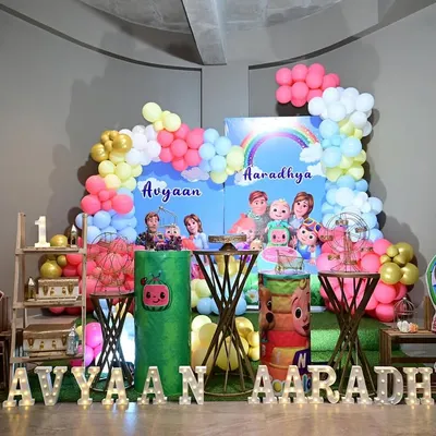 A bright and cheerful Cocomelon theme for a joint birthday party. The setup includes a custom backdrop, character cutouts, and themed cake tables.