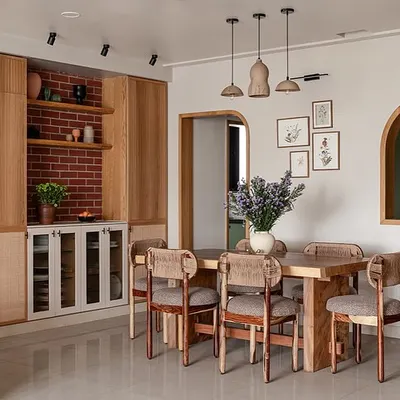 This dining area flows seamlessly from the living room, anchored by a custom live-edge dining table and rounded chairs. The crockery unit features a mix of fluted and cane details, while a brick-clad niche adds rustic charm.