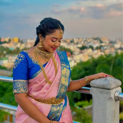 A beautiful model shoot featuring a traditional South Indian look. I paired a pink and blue silk saree with heavy gold jewelry, a braided hairstyle, and makeup featuring a sharp wing and red lips.