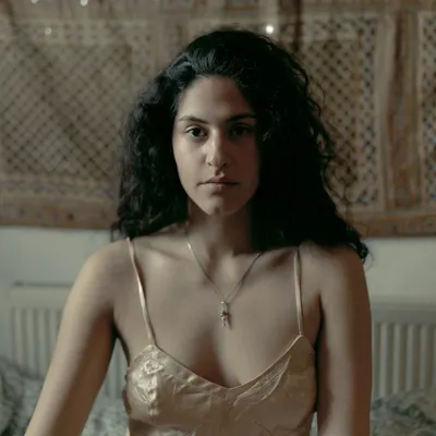 An intimate portrait of Riya Miam in her London home, capturing a quiet and direct gaze in a soft, natural light setting.