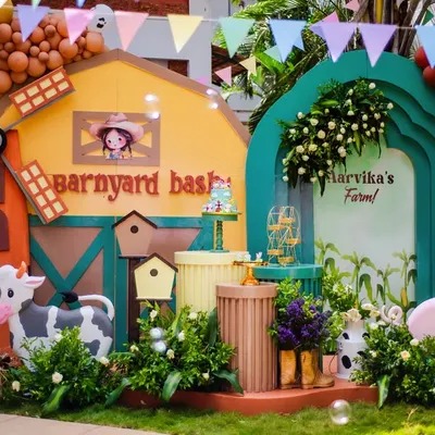 Welcome to Aarvika's Barnyard Bash! This full stage setup features a colorful barn, a windmill, and adorable cow and pig props, all surrounded by bubble machines for extra fun.