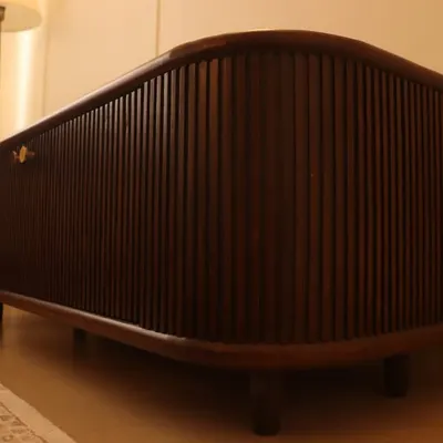 This custom-built console features a dark wood finish and a fluted, curved facade. The clean lines and retro-style legs create a sophisticated, mid-century modern piece that adds elegance to any room.