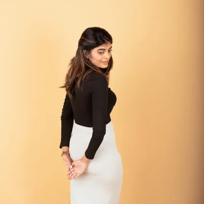 A chic and modern studio portrait. The simple beige background and clean outfit create a sophisticated look perfect for a professional profile or personal branding.