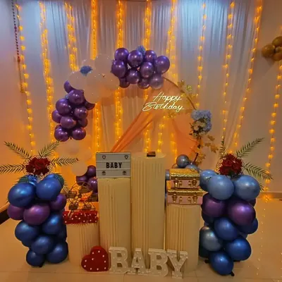 A lovely setup perfect for a baby shower or naming ceremony. The decor features blue and purple balloons, "BABY" light-up letters, and plinth stands for gifts or a cake.
