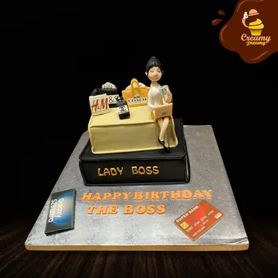 For the "Lady Boss" who does it all. This cake celebrates success with fondant figures of a boss lady, shopping bags from brands like H&M and Coach, a phone, and a credit card.