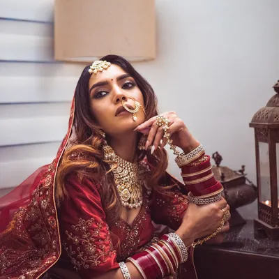 A modern bride with a traditional soul. Her direct gaze and confident pose are balanced by the classic bridal attire, including the intricate nath and maang tikka, creating a powerful and contemporary bridal portrait.