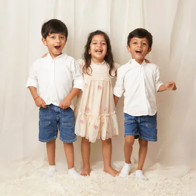 Three older siblings stand together, laughing with wide-open mouths. This candid shot captures the pure joy and energy of their relationship.