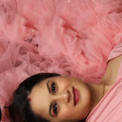 A close-up portrait focusing on the serene expression and flawless makeup of the mom-to-be, surrounded by a cloud of soft pink tulle.