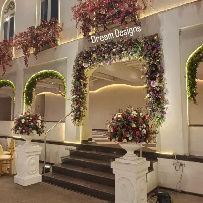 A beautiful floral entrance designed to complement the venue's architecture. The arch is covered in a rich tapestry of purple and red flowers, with matching arrangements in classic white urns.