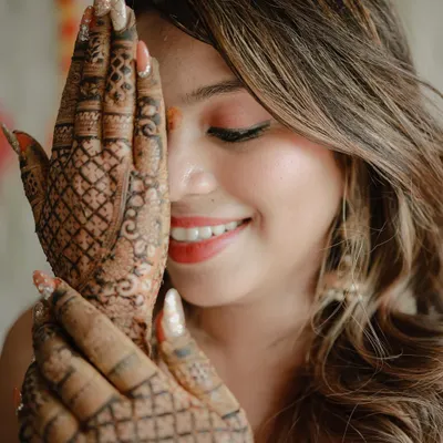 A close-up portrait focusing on the bride's beautiful smile and her intricate mehndi design. This shot captures her happiness and the artistry of the henna.