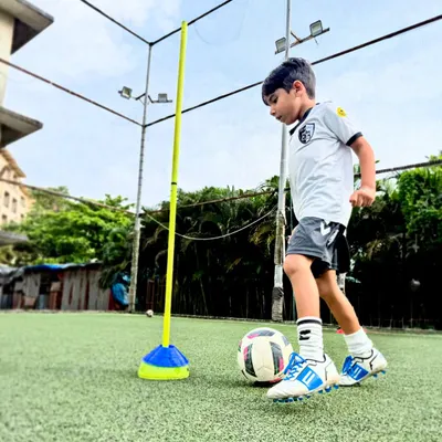 A young player focuses on close control while navigating an agility pole, a core drill for improving dribbling in tight spaces.