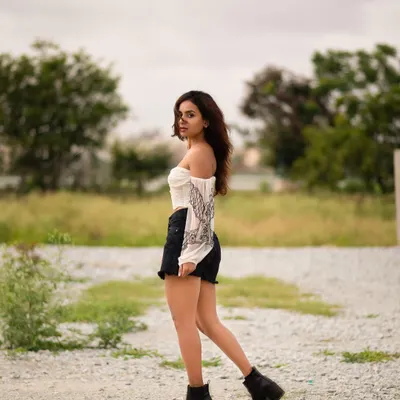 An outdoor portrait set in a field, capturing a candid, windswept moment. The natural setting and casual styling create a feeling of freedom and raw beauty.