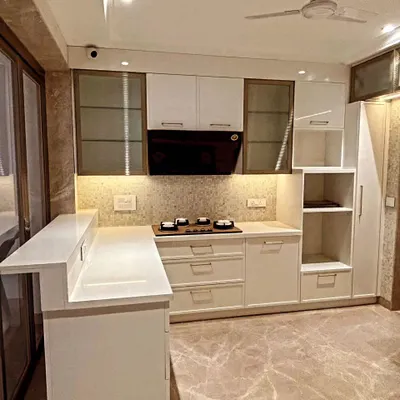 An overview of a beautiful L-shaped kitchen with a breakfast counter. The design combines white cabinets with frosted glass upper units and a textured mosaic backsplash.