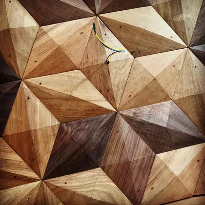 A close-up of a 3D geometric wall panel crafted from different shades of wood. This type of detailed woodwork adds texture, depth, and a unique artistic touch to our interior projects.
