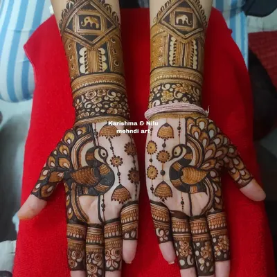 A classic guest mehendi design featuring symmetrical peacocks and hanging jhumkas. The palace or 'jharokha' motif at the wrist adds a touch of royal elegance.
