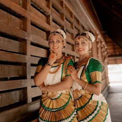 A beautiful portrait of two Mohiniyattam dancers. The composition highlights their synchronized costumes and graceful poses against a traditional architectural background.