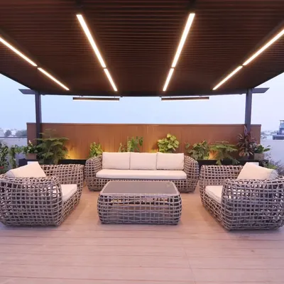 A completed pergola lounge in Palam Vihar, Gurgaon, with modern wicker furniture and integrated ceiling lights. The raised wooden deck clearly defines the seating area.