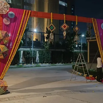 This is a festive gate I designed for a Mehendi or Sangeet night. It features a bright pink and orange fabric frame, decorated with marigold flower strings, paper pinwheels, and hanging Rajasthani umbrellas.