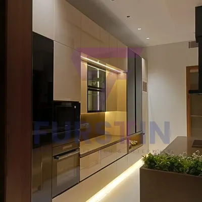 A perspective of the Bharatpur island kitchen, highlighting the seamless, handle-less drawers and the built-in wall oven. The warm, ambient lighting under the cabinets and along the floor creates a sophisticated glow, making the kitchen feel both modern and welcoming.