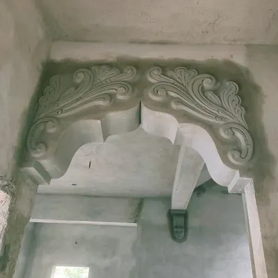 A grand, ornate archway sculpted in cement, designed to be the centerpiece of a hall. The intricate floral patterns and curved supports add a royal feel to the interior space.