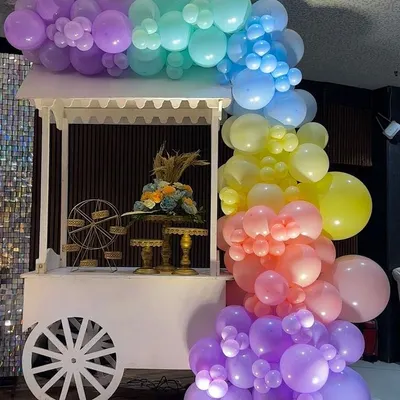 A charming white cart decorated with a pastel rainbow balloon garland, used as a dessert station for a beautiful baby shower.