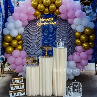 This elegant birthday backdrop combines multiple elements for a rich, textured look. A balloon arch in pink, white, and gold frames a royal blue and white draped background, creating a luxurious setting for the celebration.