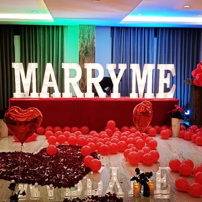 I designed this grand proposal setup in a hotel room, using large marquee letters to create a bold and unforgettable 'MARRY ME' moment. The decor features a classic romantic theme with a dense path of red rose petals, heart-shaped foil balloons, and dramatic lighting to make the occasion truly special.