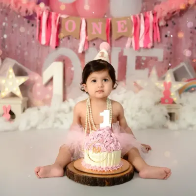 A classic first birthday cake smash portrait. This little girl is ready to celebrate with her pink rosette cake, wearing a party hat and pearls.